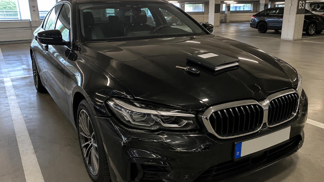 Schwarzer Firmenwagen mit Frontschaden in einer Tiefgarage, Schlüssel und Unterlagen auf der Motorhaube