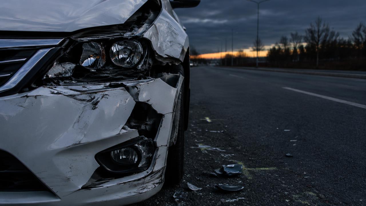 Beschädigte Front eines weißen Autos mit Splittern auf der leeren Straße in der Dämmerung